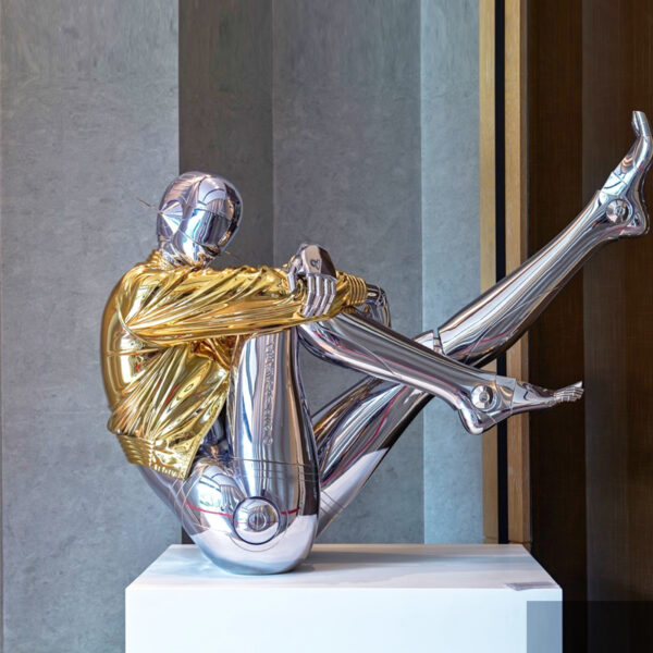 Chrome robot sculpture lamp in gold jacket sitting on a pedestal with LED lighting.